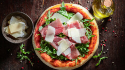 Fersk pizza Parma med parmesanost og parmaskinke på trebord