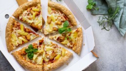 Pizza Hawaiian i en pappeske på en lys stein eller betong bakgrunn. Plass til tekst. Topp utsikt. Pizza levering. Pizzameny.